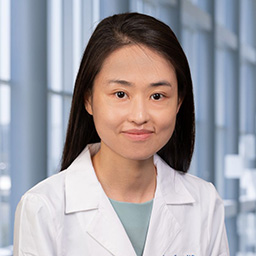 Dr. June Song wearing a light blue shirt, and a white lab coat standing in the Clements University Hospital lobby