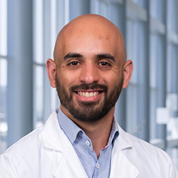 Dr. Mustafa Ghanem wearing a blue shirt and a white lab coat standing in the Clements University Hospital lobby