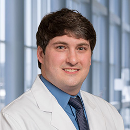 Dr. Cameron Landers wearing glasses, a blue shirt with a patterned tie and a white lab coat standing in the Clements University Hospital lobby