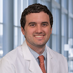 Dr. Miguel Ortiz Bezara wearing a blue shirt with a red patterned tie and a white lab coat standing in the Clements University Hospital lobby.