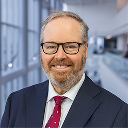 Dr. Joshua Beckman wearing glasses, a dark suit with red tie in the Clements University Hospital lobby
