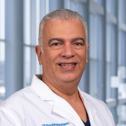 Dr. Ghassan Elkadi wearing a white lab coat, standing in the CUH lobby