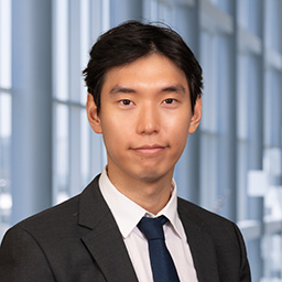 Dr. Jiho Sohn wearing a white shirt with a black tie and black suit jacket standing in the Clements University Hospital lobby