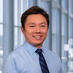 Dr. Kohei Suzuki wearing a blue shirt and blue striped tie standing in the Clements University Hospital lobby