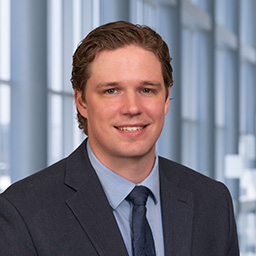 Dr. Adam Wolf wearing a blue shirt and tie with a dark suit coat standing in the Clements University Hospital lobby