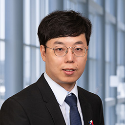 Dr. Hanghang Zhang wearing glasses and a white shirt dark tie and suit coat standing in the Clements University Hospital lobby