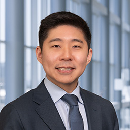 Dr. Eliot Zhu wearing a light grey shirt with dark grey tie and suti jacket standing in the Clements University Hospital lobby