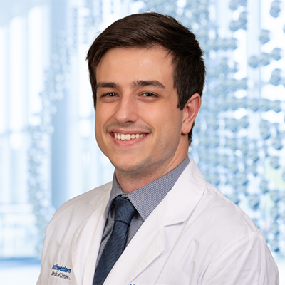 Dr. Nil Saez Celveras wearing a blue shirt witha blue necktie and a white lab coat, standing in the Clements University Hospital lobby 