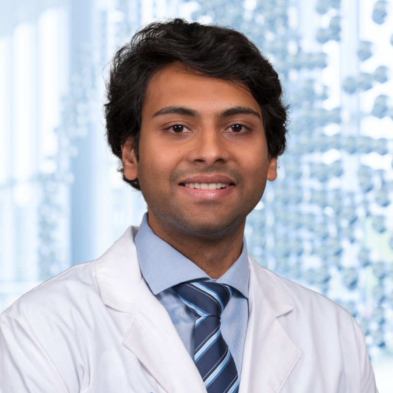 Dr. Vinayak Subramanian wearing a blue shirt with a stiped blue necktie and a white lab coat, standing in the Clements University Hospital lobby