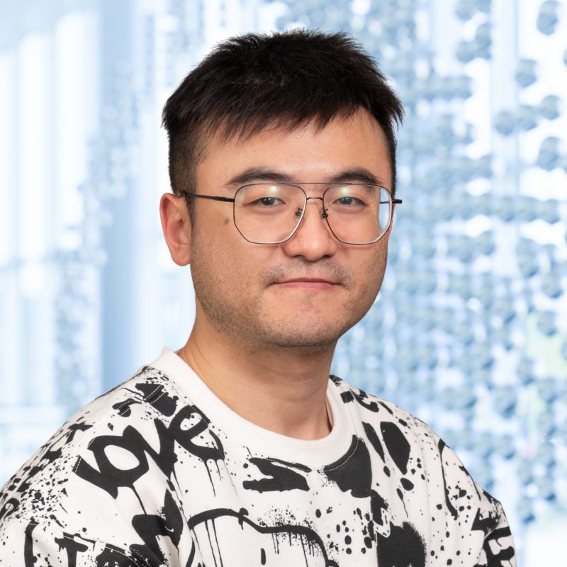 Dr. Baije Xu wearing glasses and a black and white sweatshirt, standing in the Clements University Hospital lobby