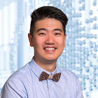 Dr. Haitao Xu wearing a blue shirt with a wooden bow tie, standing in the Clements University Hospital lobby