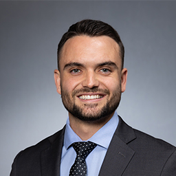 Joseph Campaign wearing a dark suit with light blue shirt and dark necktie