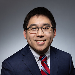 Michael Li wearing glasses, a white shirt with red and blue stripped necktie and a darl blue jacket