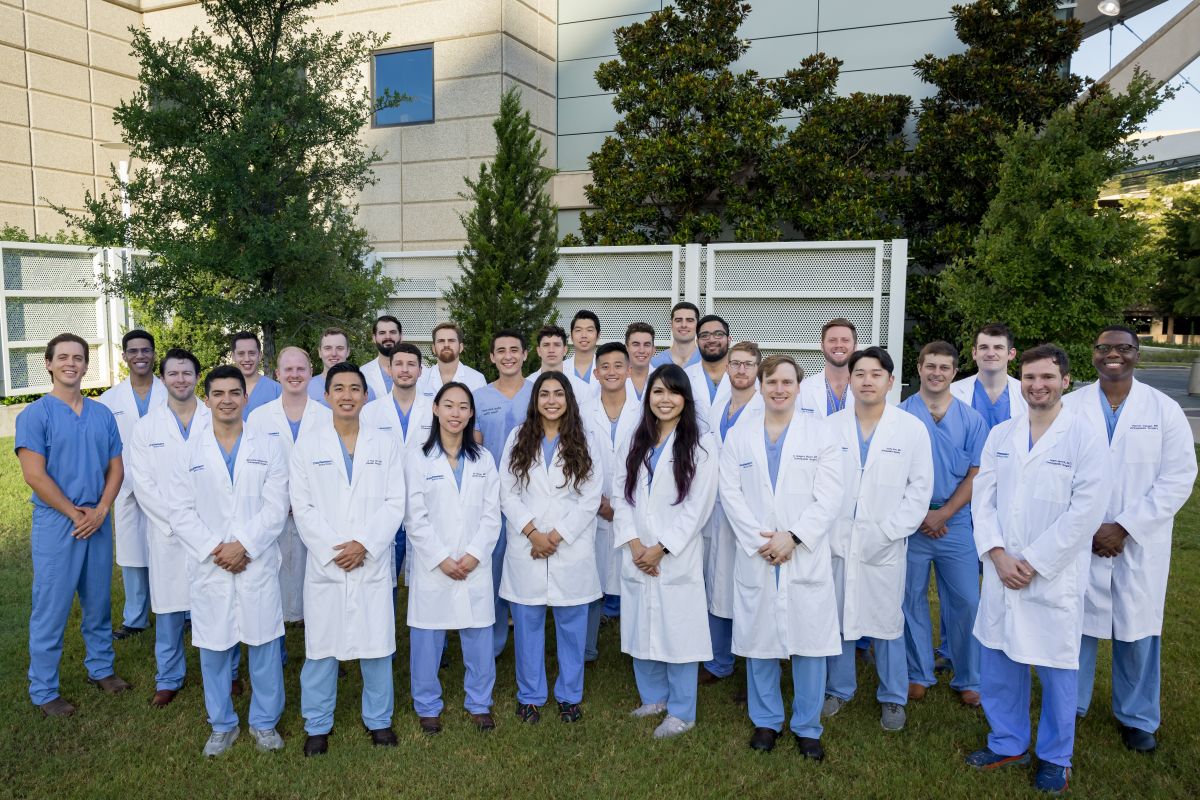 group of 30 Orthopaedic Surgery Residents in white coats and blue scrubs standing outside hospital