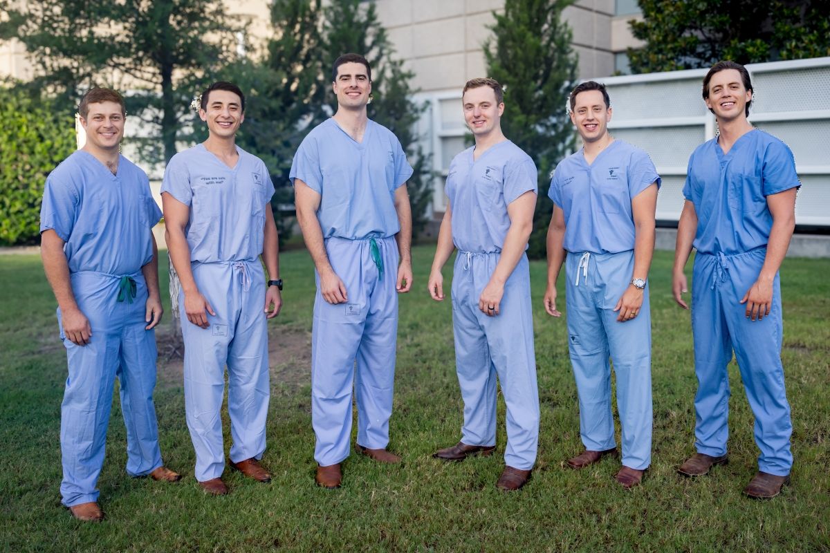 group of 6 male Orthopaedic Surgery Residents weariing blue scrubs standing outside hospital