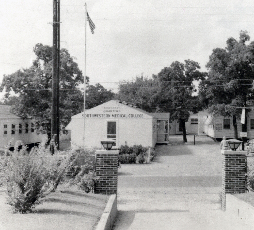 UT Southwestern Medical School in 1943 UTSW Medical School 1943 single story building in center of walkway with shrubs and flagpole at left