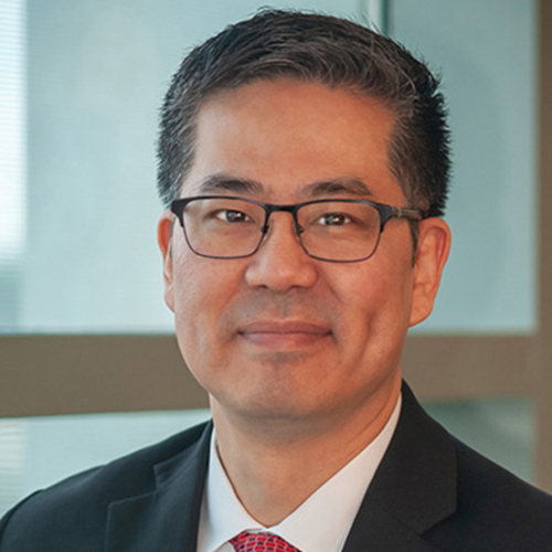 Dr. Kim, a smiling man with dark hair, wearing a dark suit and glasses.