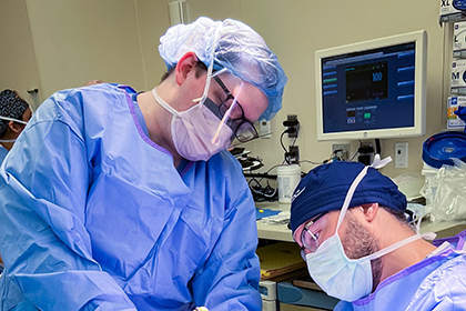 Two doctors wearing scrubs and masks bending over a patient.