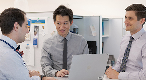 Three male residents conversing around a laptop
