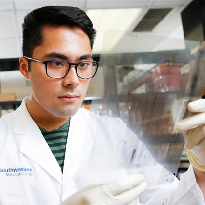 A man in a white lab coat looks at data on a clear sheet