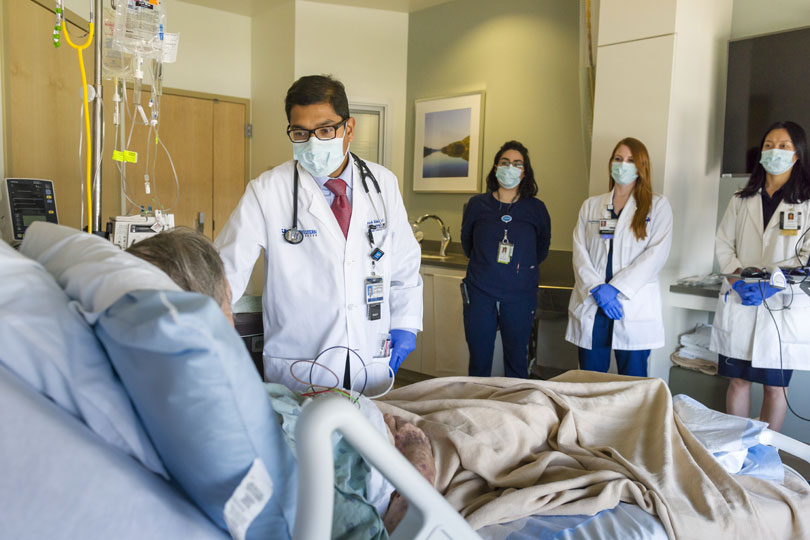 A faculty member and student tend to a patient. An attending physician and students wear masks as they attend to a patient in a hospital