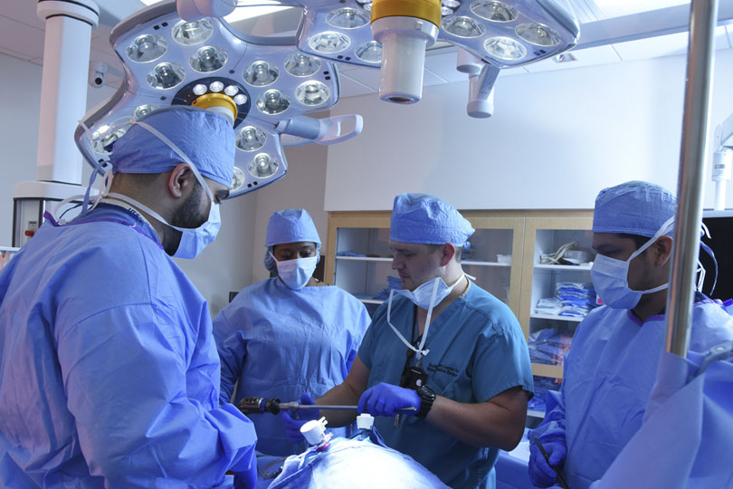 Students practice surgery in the Simulation Center. Students in masks and gowns practice surgery in the Simulation Center