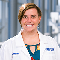 woman with short brown hair wearing an aqua colored shirt and white coat with UT Southwestern Medical Center logo