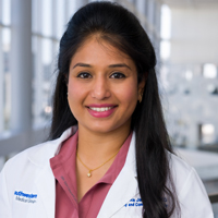 woman with long, dark hair wearing a pink shirt and white coat