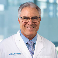 man with grey hair wearing a light blue shirt, blue striped tie, and white coat
