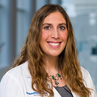 woman with long, wavy brown hair wearing a green shirt and white coat