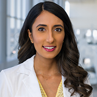 woman with long, dark hair wearing a yellow shirt and white coat