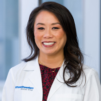 woman with long, dark hair wearing a red and black patterned shirt and a white coat with the UT Southwestern Medical Center logo