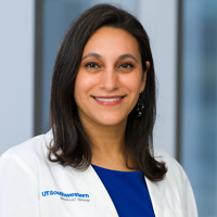 woman with shoulder-length dark hair wearing a royal blue shirt and white coat with UT Southwestern Medical Center logo