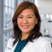 woman with shoulder-length brown hair wearing an teal green shirt and white coat