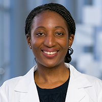 woman with black hair worn in braids wearing a black shirt and white coat
