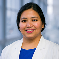 woman with long dark hair pulled back in a bun wearing a royal blue shirt and white coat