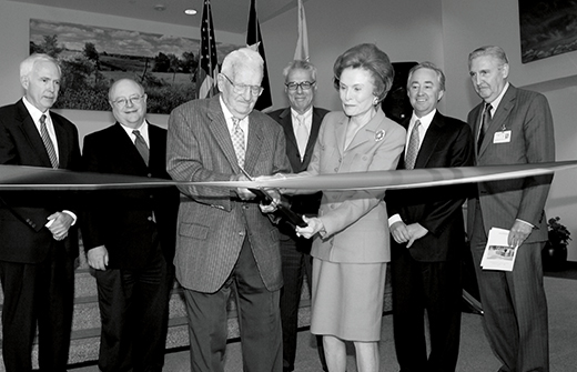 Bill and Rita Clements at Ribbon-Cutting Ceremony Bill Clements cuts ribbon with ceremonial scissors as Rita Clements assists and dignitaries look on