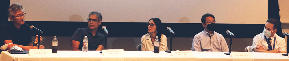 Integrating research and patient care panel discussion. Five panel members seated at a long table listening as one member speaks
