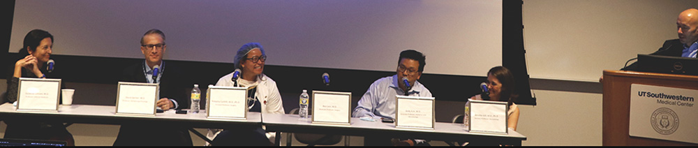 Integrating research and patient care panel discussion. Five person panel seated at long table with one person standing at podium to right of table