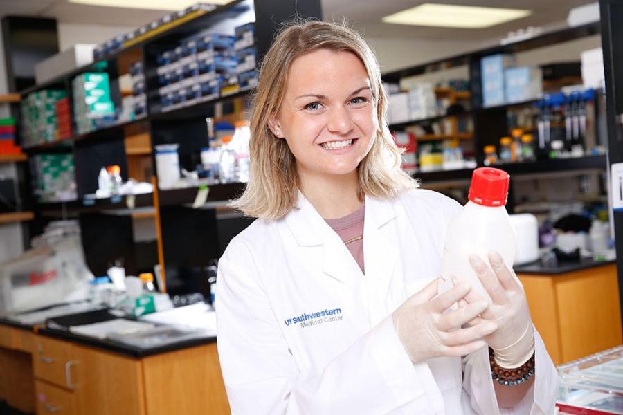 young blond woman medical researcher wears white coat and holds plastic bottle