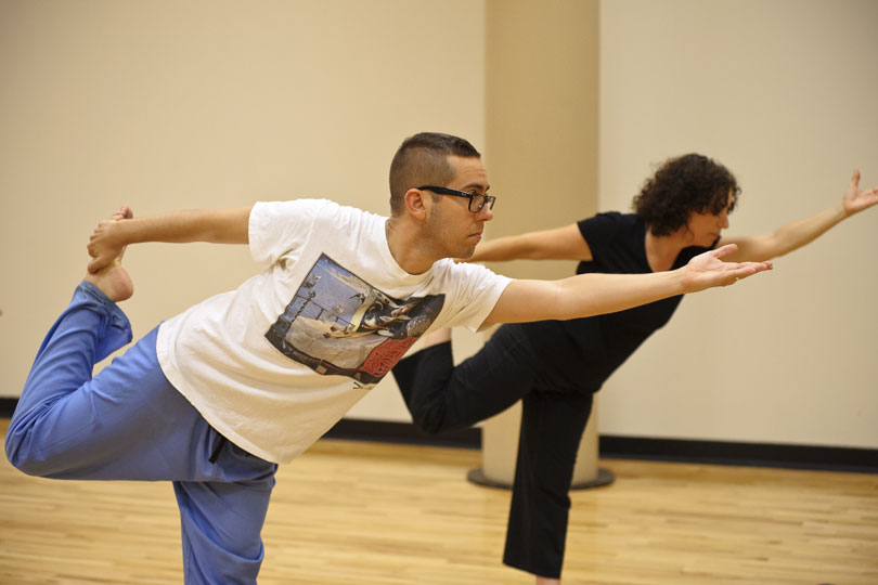 Two people do the dancer pose in a yoga class. A man and a woman stand on one leg and stretch in the dancer pose during a yoga class m