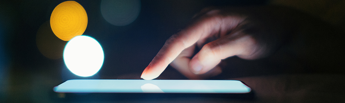 hand touches lit cellphone screen against dark background