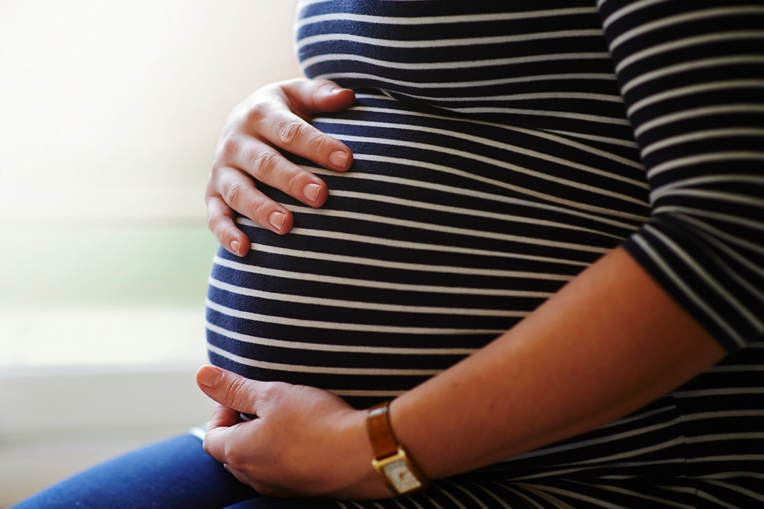 Heavily pregnant female sitting by window, holding her bump with both hands.