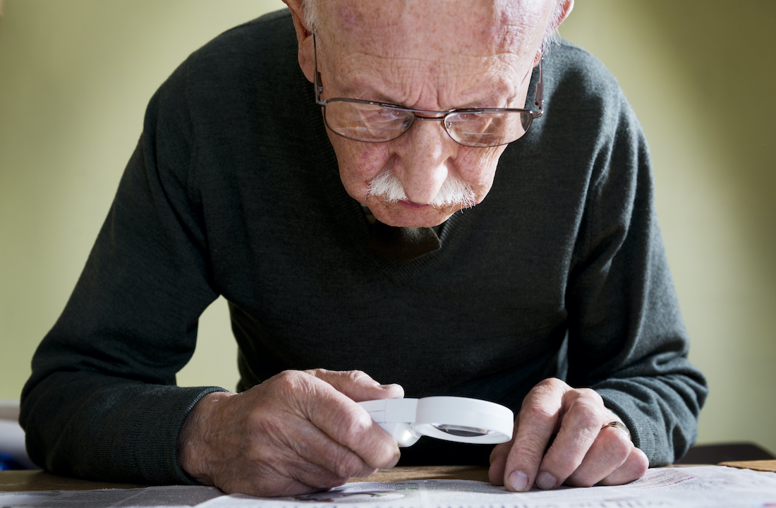 A patient with wet age-related macular degeneration (AMD) uses an illuminated magnifying glass to read.