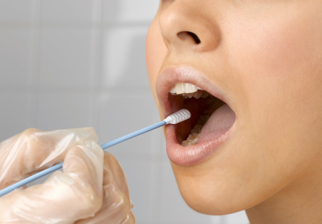 Person holding DNA swab in young woman's mouth, close up of mouth, studio shot