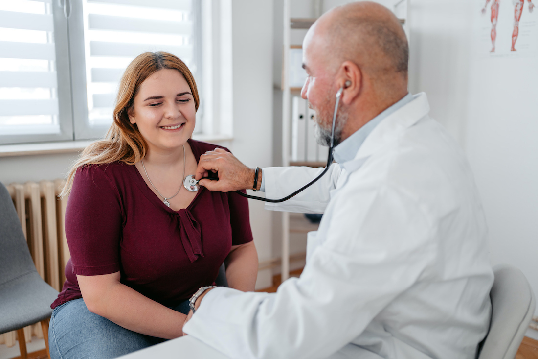 Senior male doctor auscultating a female patient.