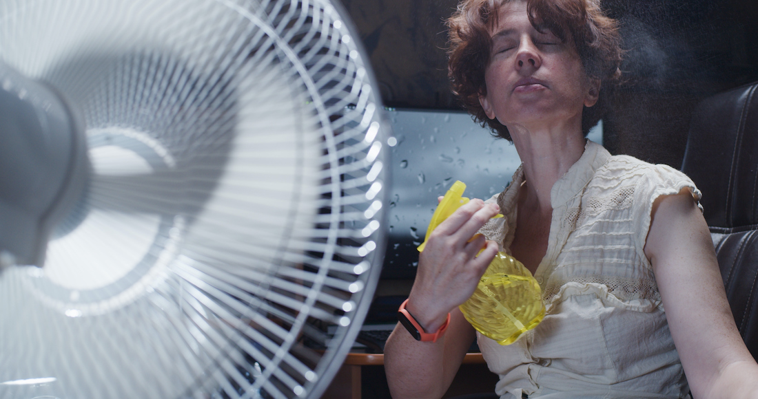 Woman is trying to work at the desktop computer at home, suffering from hot weather and spraying water onto her face while using electric fan