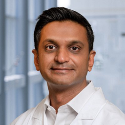 Dr. Suraj Patel wearing a white shirt and a white lab coat standing in the Clements University Hospital lobby